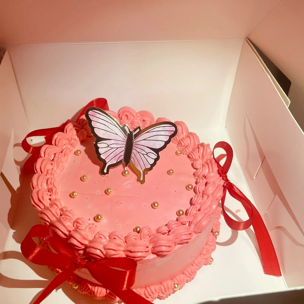 Pink buttercream cake with red ribbon bows, gold pearls and large butterfly topper