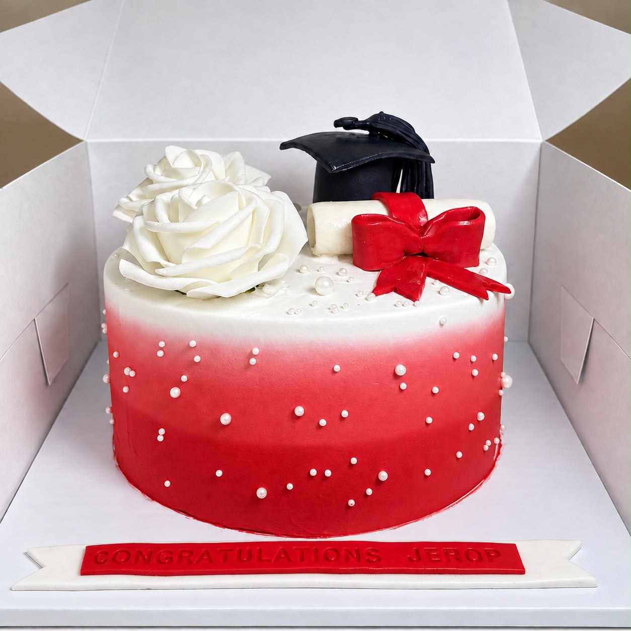 Red and white graduation cake with black cap, diploma, red bow and white roses by Moh Bakes & Treats
