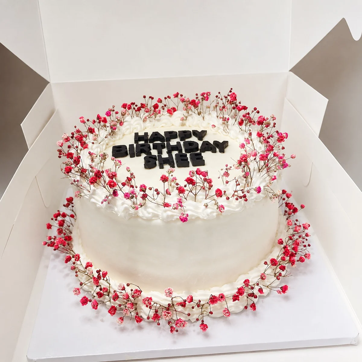 White round cake with pink floral decoration and dark lettering by Moh Bakes & Treats